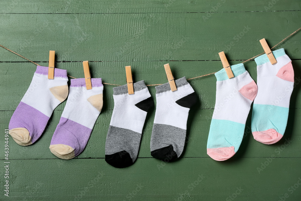 Different socks hanging on rope against green wooden background