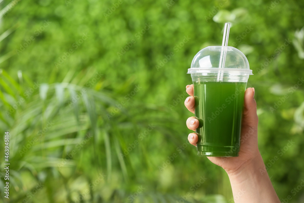 Female hand with plastic cup of healthy juice outdoors, closeup