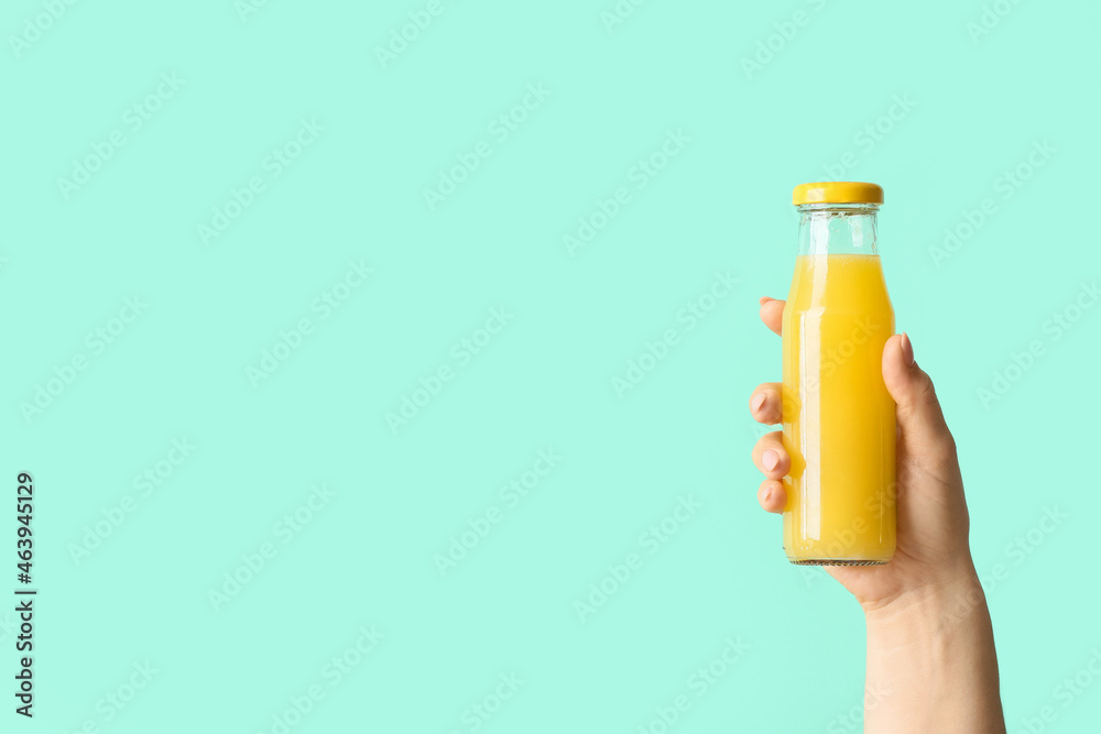 Female hand with bottle of healthy juice on color background