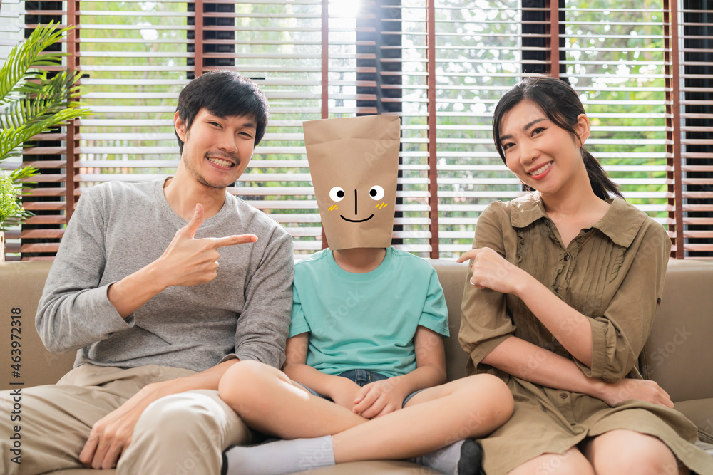 concept of family face emotions,funny humor dad mom hand pointing to his son wearing paper bag with 