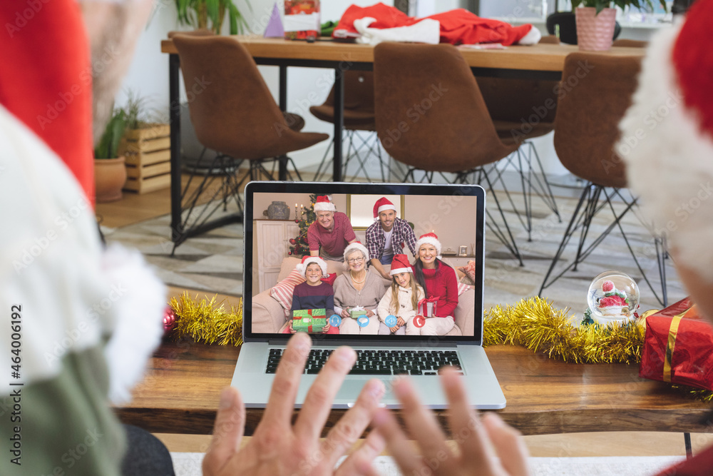 Caucasian father and son in santa hats on christmas laptop video call with smiling family