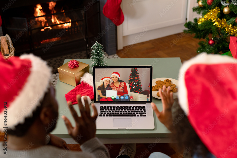 African american couple in santa hats on laptop christmas video call with friends