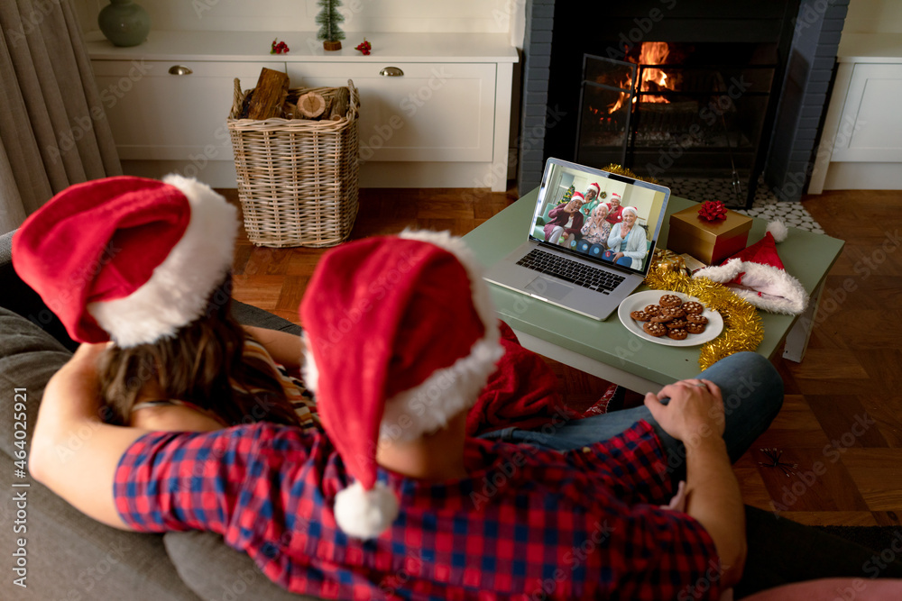 Caucasian couple in santa hats on laptop christmas video call with friedns