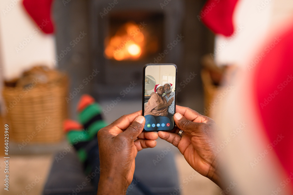 African american man in santa hat on smartphone christmas video call with smiling couple