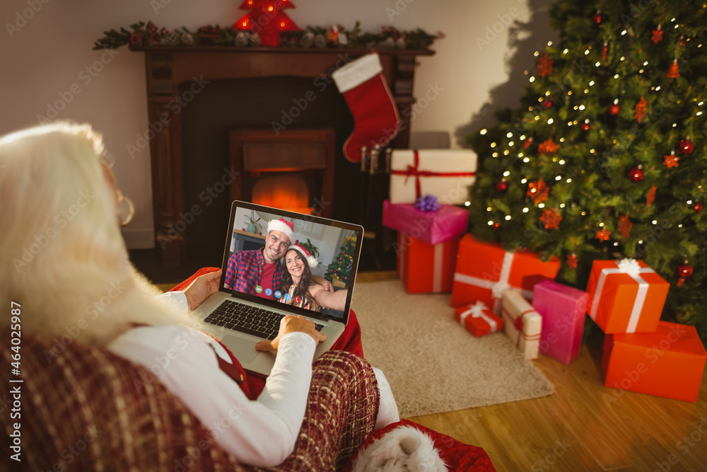 Santa claus on christmas laptop video call with smiling caucasian couple