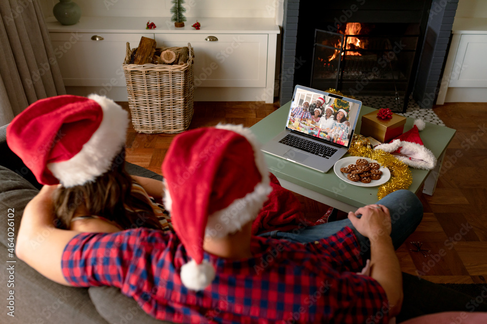 Embracing caucasian couple making laptop christmas video call with smiling african american family