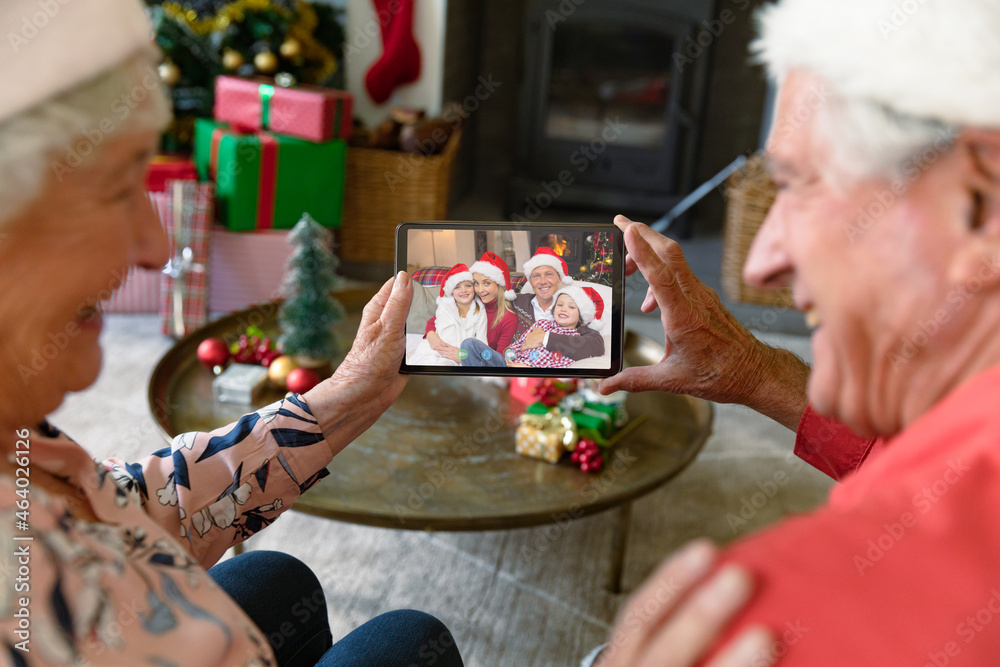 Happy caucasian senior couple making tablet christmas video call with smiling family