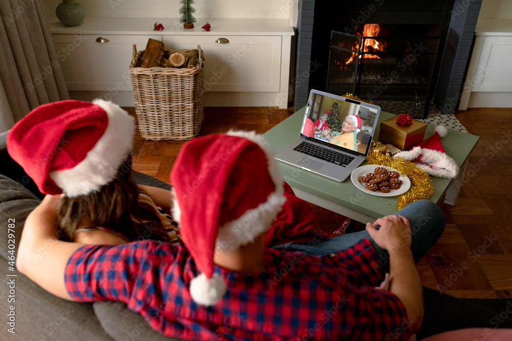 Caucasian couple in santa hats on christmas video call on laptop with senior parent