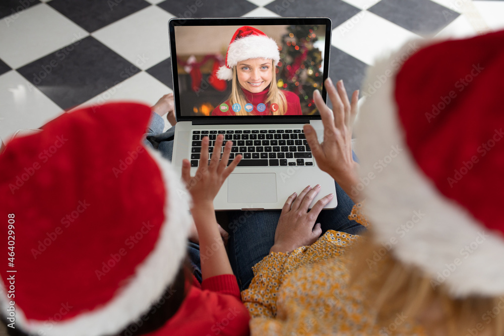 Caucasian mother and child in santa hat on christmas video call on laptop with female friend