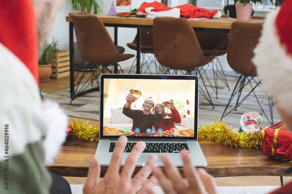 Caucasian couple in santa hat on christmas video call on laptop with caucasian couple