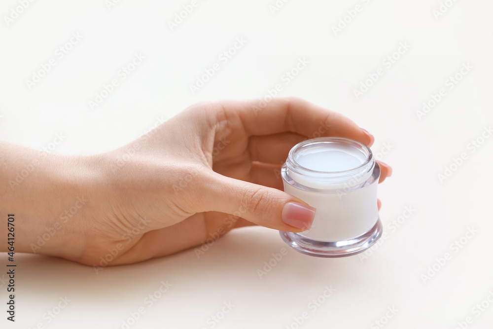 Female hand with jar of cosmetic cream on light background