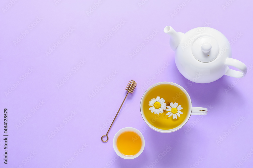 Teapot and cup of fresh chamomile tea with honey on purple background