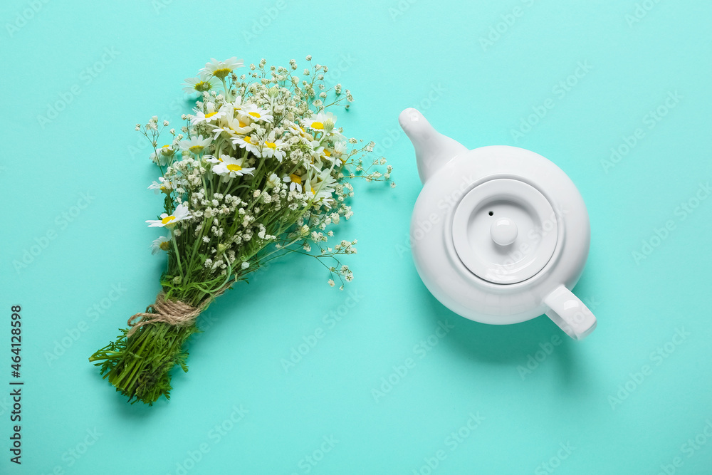 Teapot of tasty tea and chamomile flowers on color background