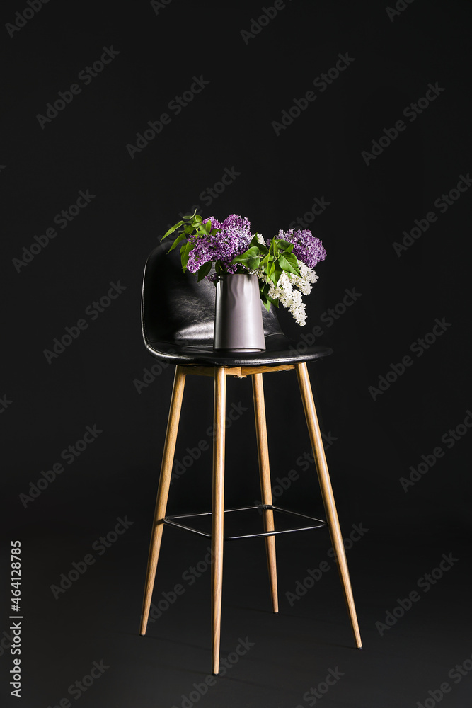 Chair with stylish vase and lilac flowers on dark background