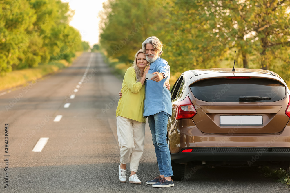 Happy mature couple taking selfie near car in countryside