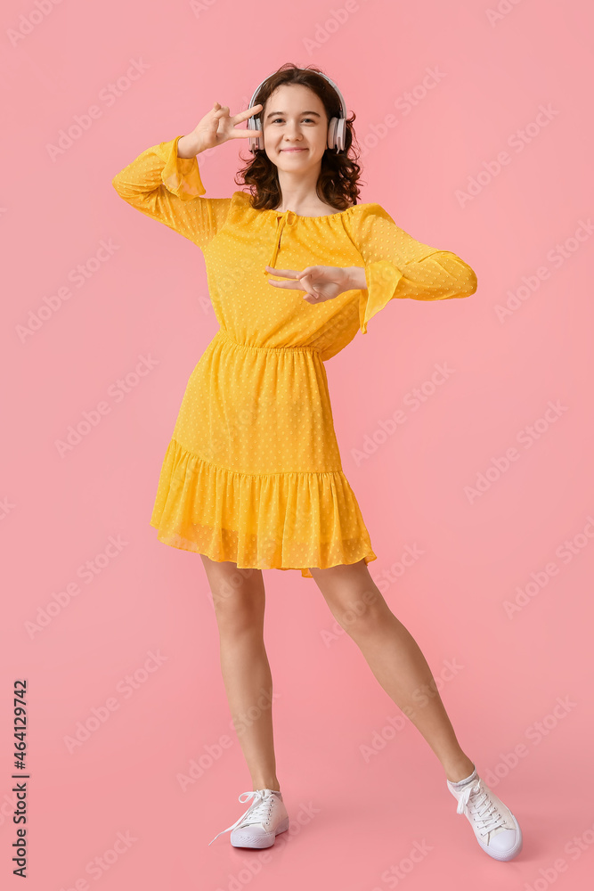 Pretty teenage girl in headphones listening to music on pink background