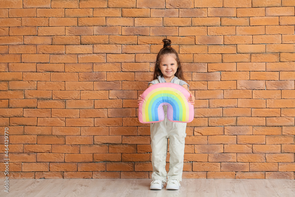 Adorable little girl with toy rainbow near brick wall