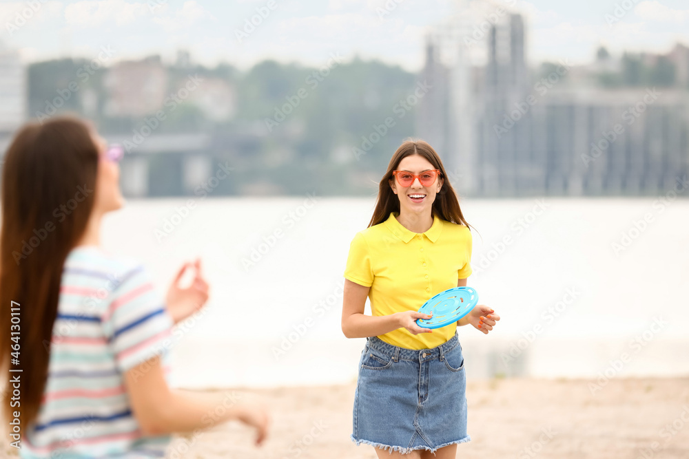 Beautiful young women playing frisbee near river