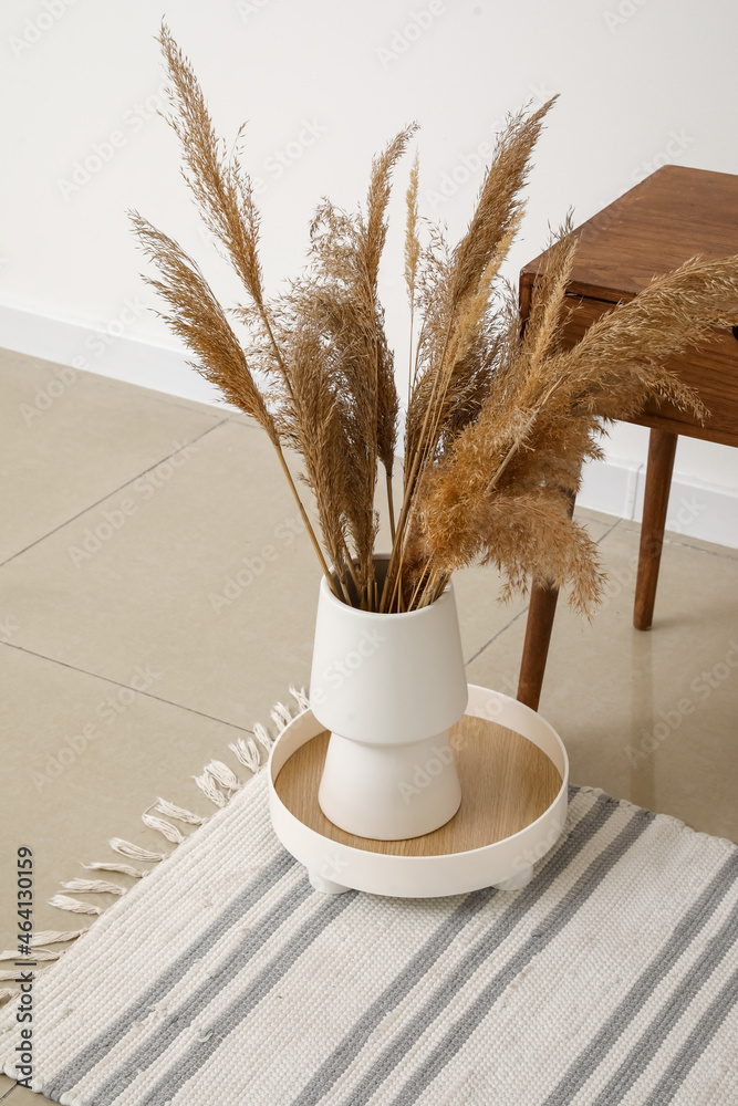 Vase with dry reeds on floor in room