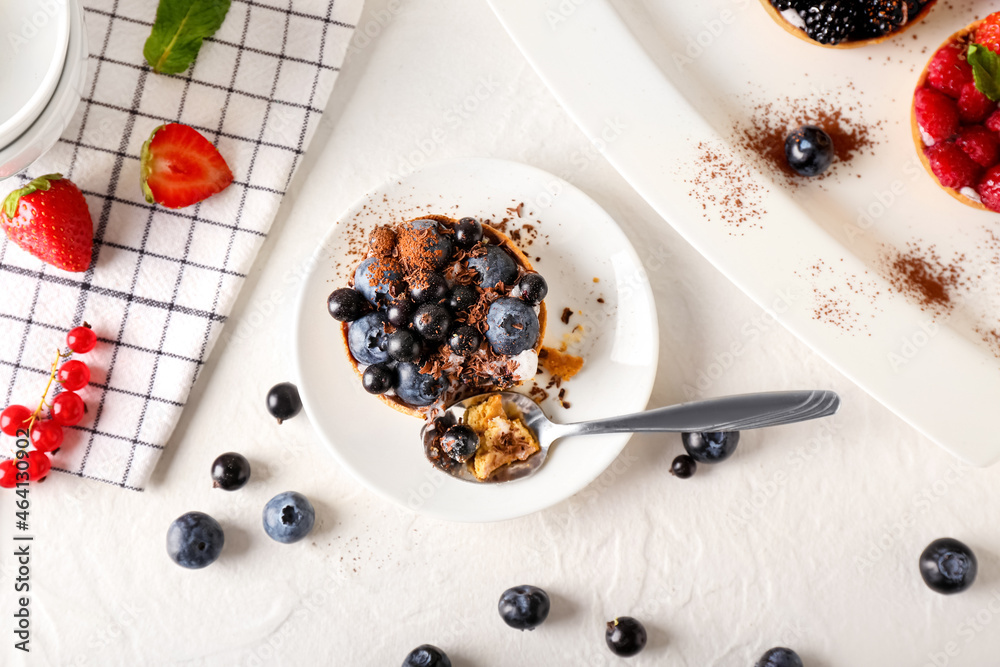 Plate with spoon and tasty berry tart on light background