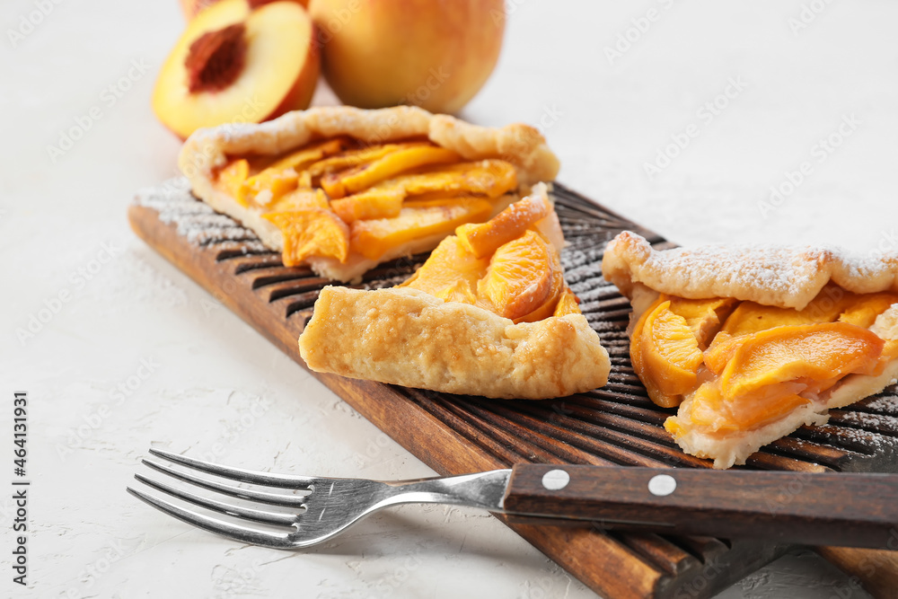 Board with pieces of tasty peach galette on light background, closeup