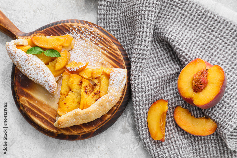 Board with pieces of tasty peach galette on light background