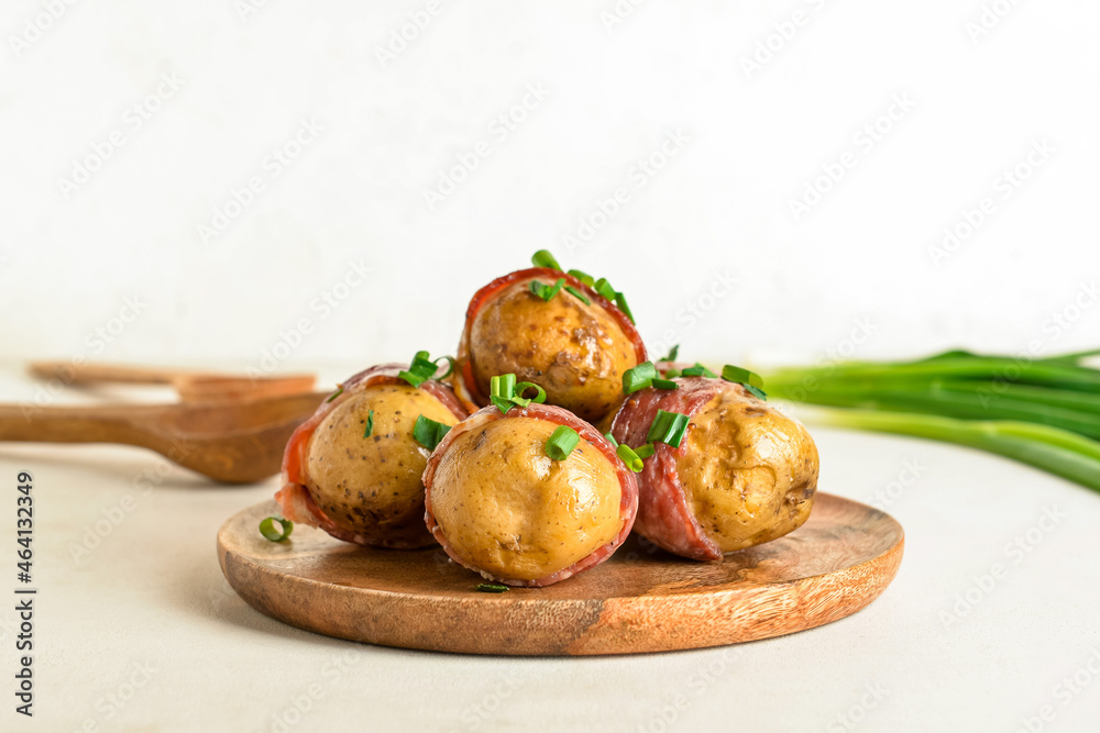 Plate of tasty baked potatoes with bacon on light background