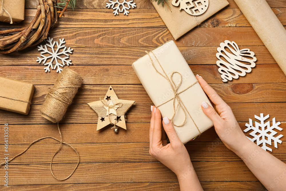 Female hands with gift box, rope and Christmas decorations on wooden background, closeup