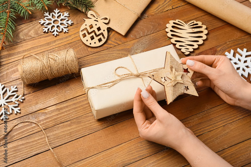 Woman making Christmas gift on wooden background, closeup