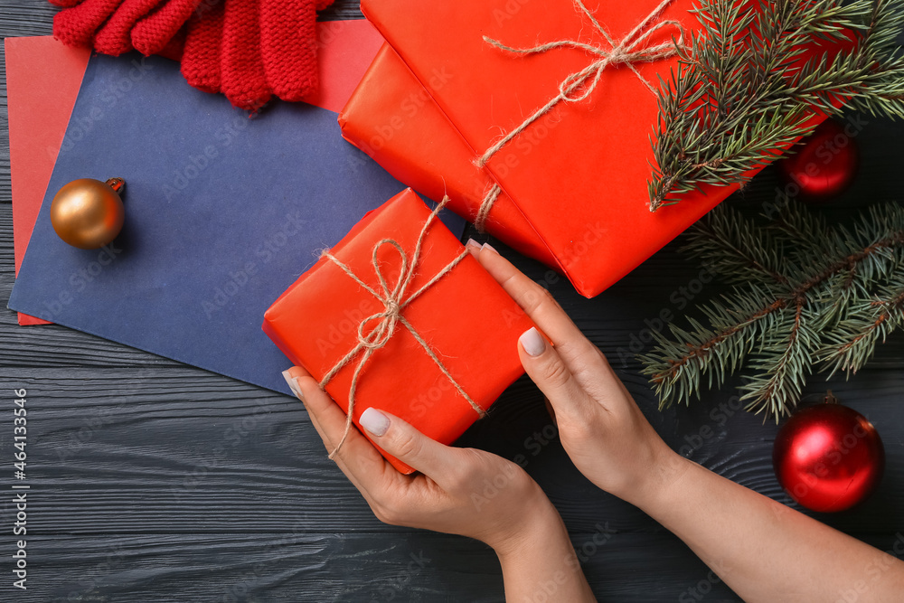 Female hands with gift boxes and color paper sheets on dark wooden background, closeup