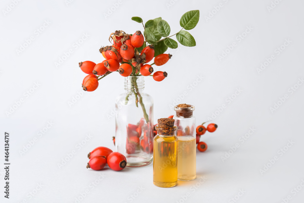 Bottles of essential oil and rose hip berries isolated on white background