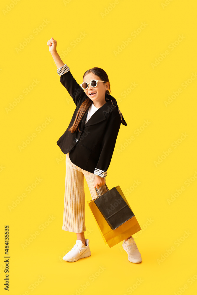 Little girl with Black Friday shopping bags on yellow background