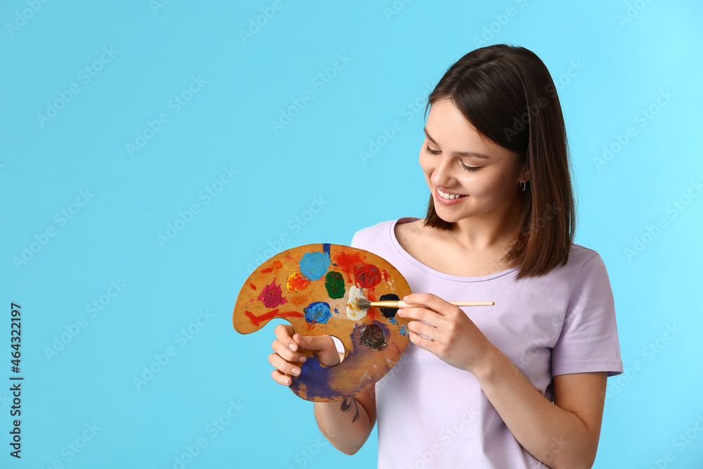 Young female artist with palette on color background