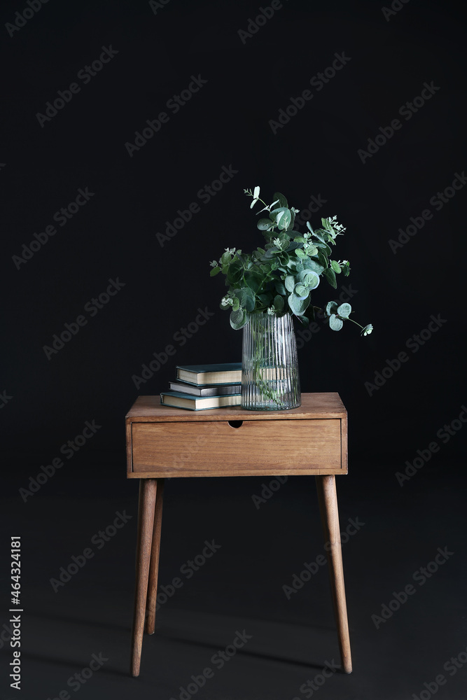 Books and vase with eucalyptus on wooden table on dark background