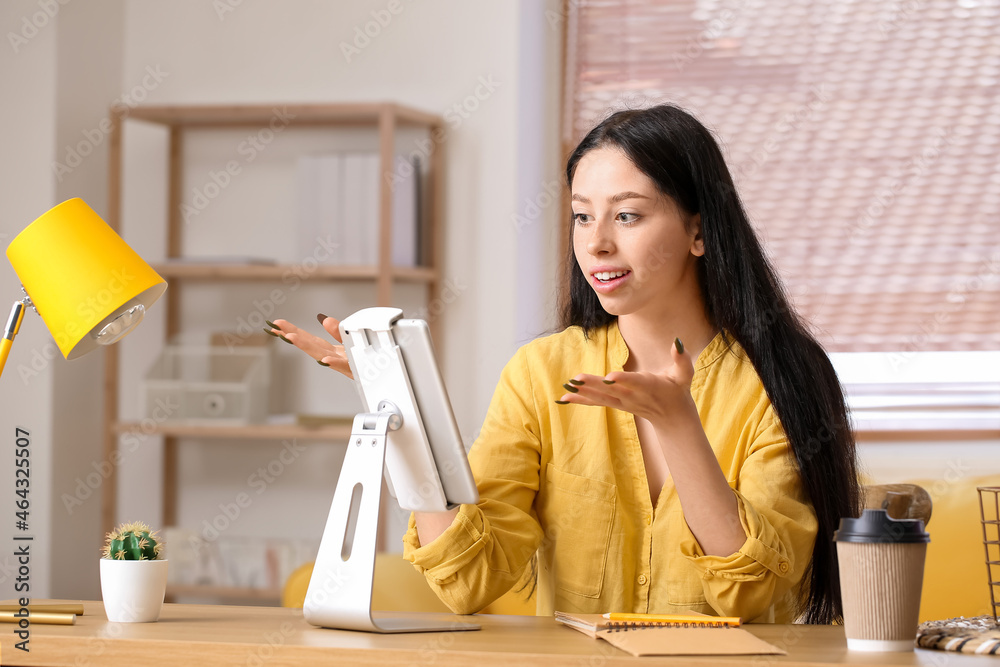 Beautiful teenage girl with tablet computer video chatting at home