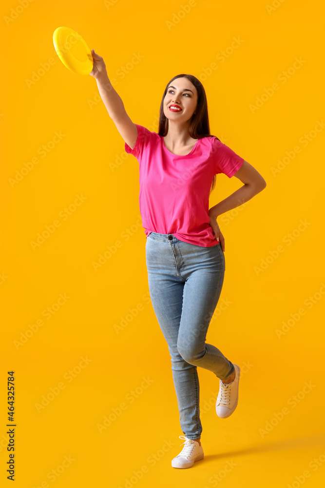 Beautiful young woman playing frisbee on color background