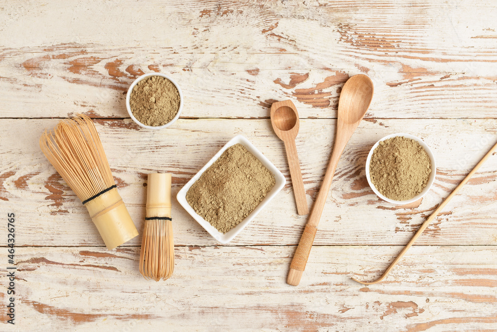 Bowls with hojicha powder, chasen, chashaku and spoons on white wooden background