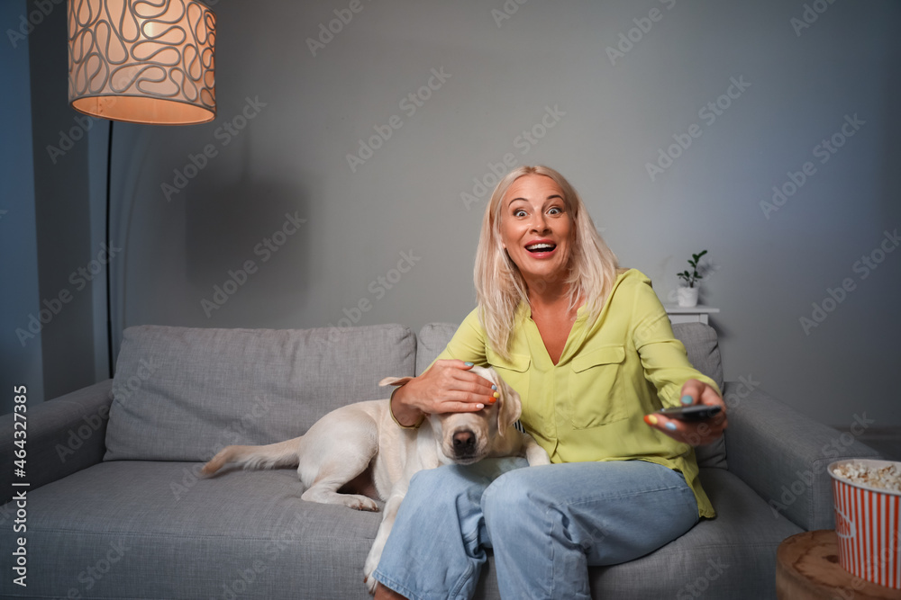 Surprised mature woman with cute Labrador dog watching TV at home