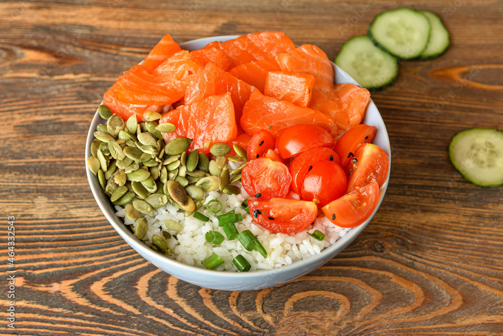 Bowl with tasty rice, salmon, tomato and pumpkin seeds on wooden background