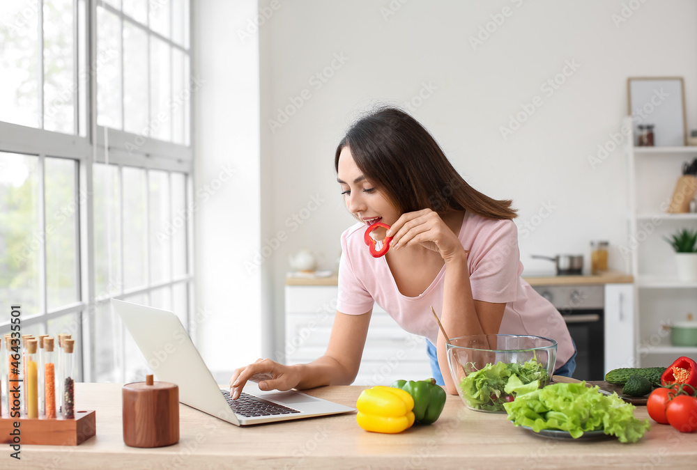 厨房里有新鲜蔬菜和笔记本电脑的年轻女人