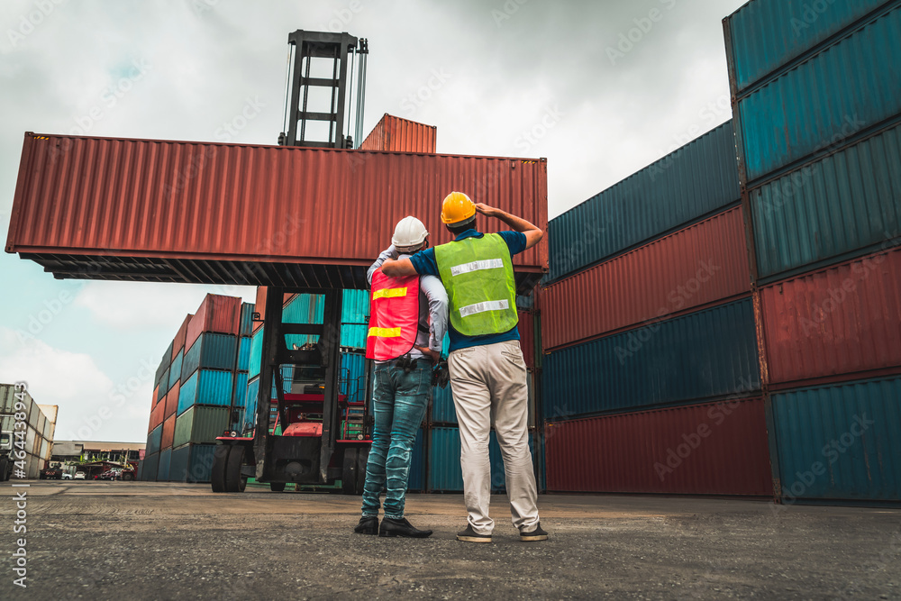 Industrial worker works with co-worker at overseas shipping container yard . Logistics supply chain 