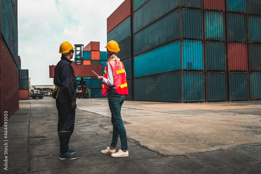 Industrial worker works with co-worker at overseas shipping container yard . Logistics supply chain 