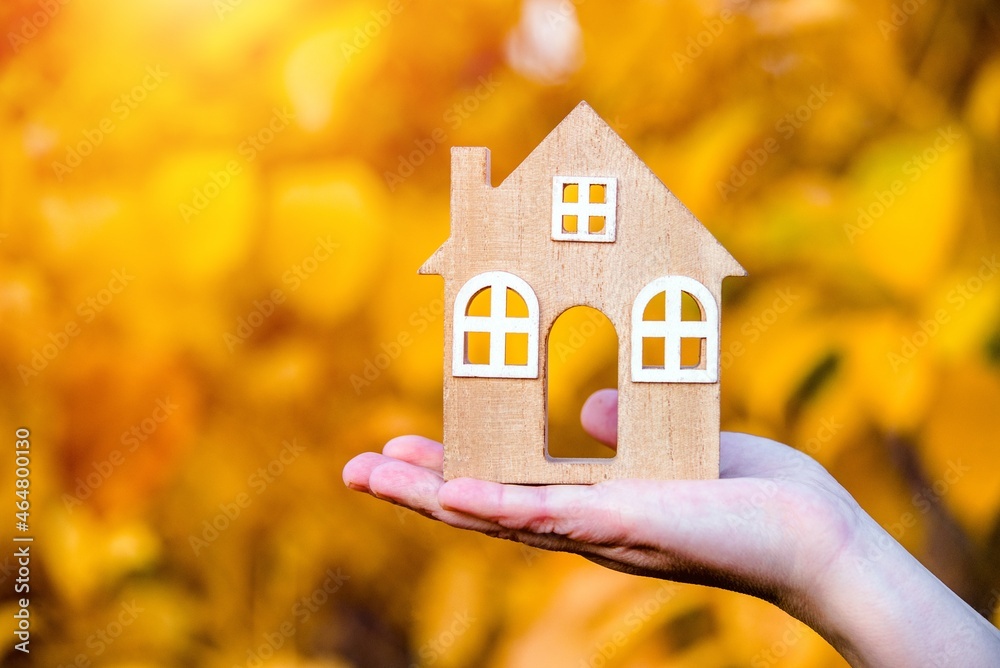 The symbol of the house in the girls hand on the background of yellow leaves