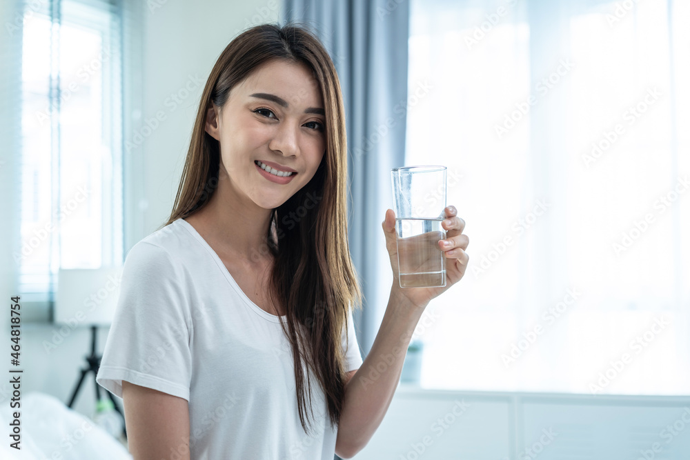 亚洲美女在卧室里拿着一杯水的肖像。