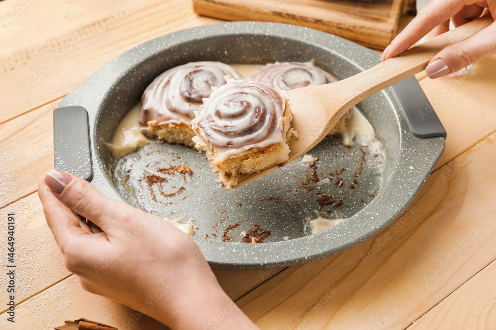 Woman taking tasty cinnamon roll from baking dish on table