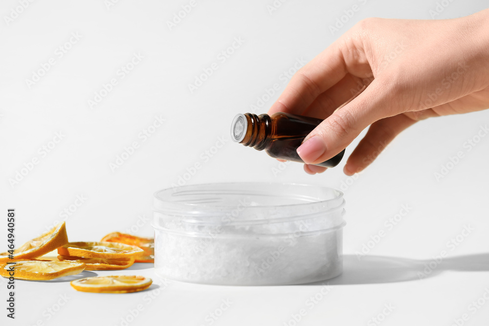 Woman adding essential oil to sea salt on light background