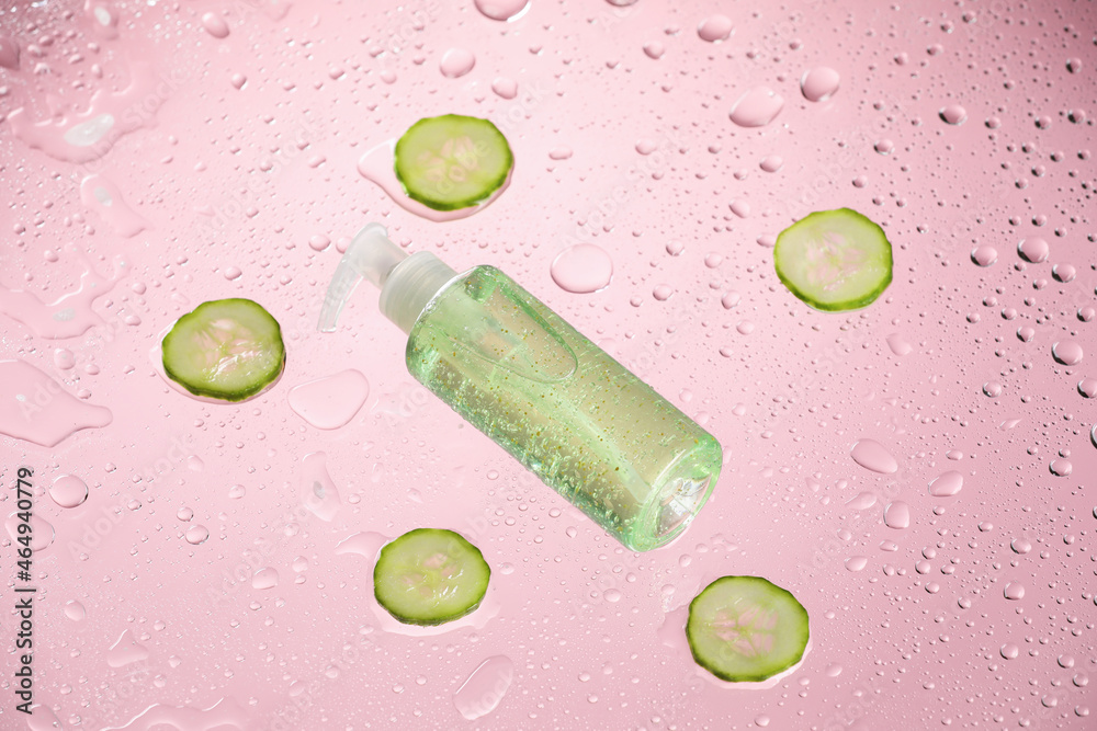 Bottle of cosmetic product and cut cucumber on color background with water drops