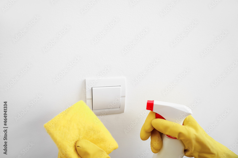 Woman cleaning switch on white wall, closeup