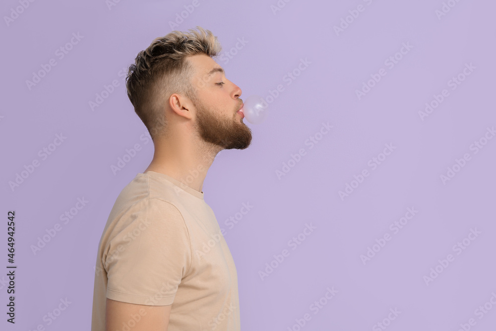 Young man with chewing gum on color background