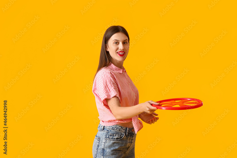 Beautiful young woman playing frisbee on color background